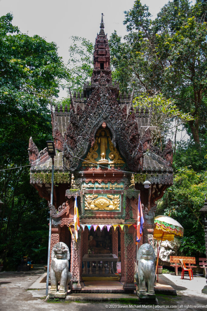 Woodland setting around an ornate shrine with Buddha image and guardian lions.