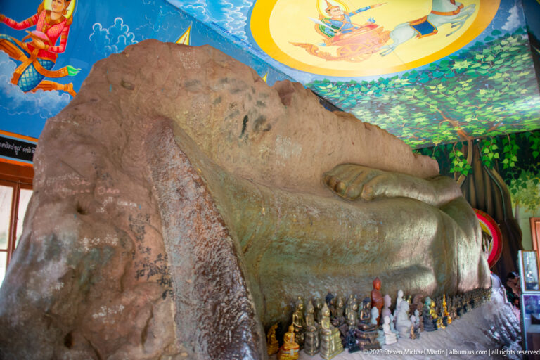 Large weathered foot of a reclining Buddha with small figures arranged along its base.