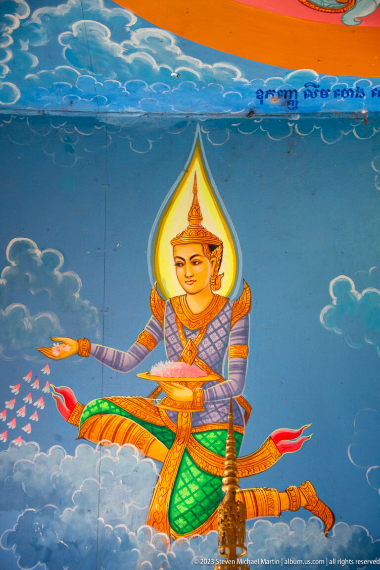 Kneeling celestial woman in a pointed headdress scattering flowers across a blue mural.