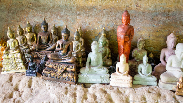 Small seated and standing Buddha figures grouped along a rough rock wall.