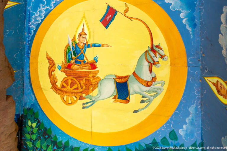 Painted figure riding a white horse-drawn chariot inside a yellow disc on a blue ceiling.