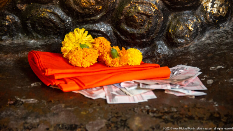 Folded orange cloth, yellow marigolds, and banknotes arranged as offerings.