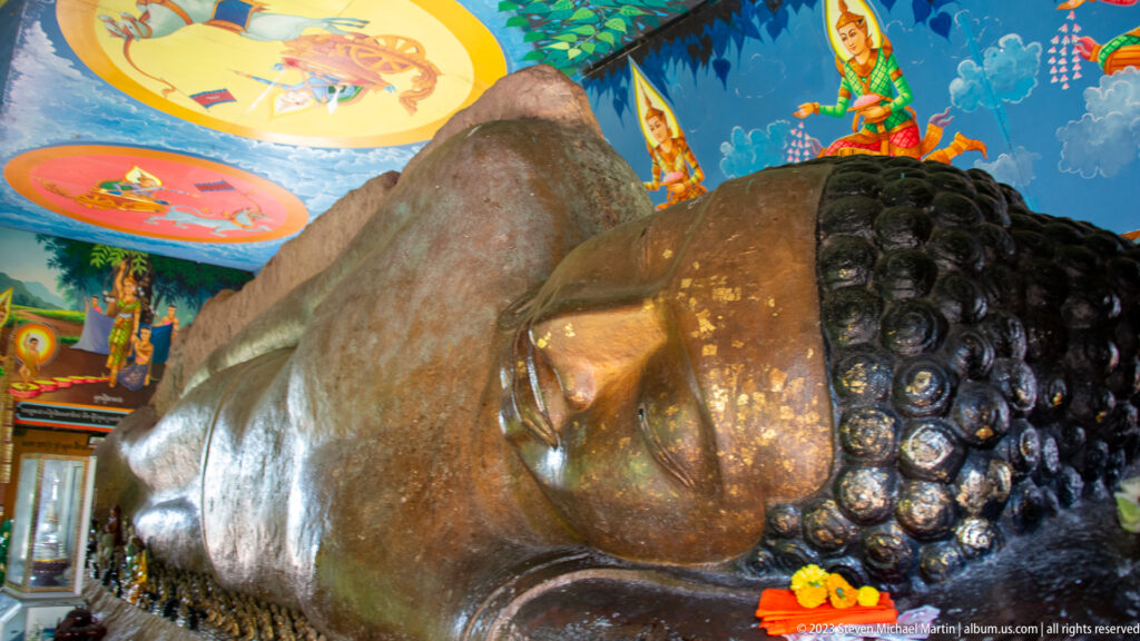 Wide angled view of the reclining Buddha with painted murals and offerings along the base.