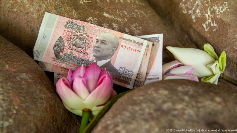 Cambodian banknote tucked among pink and white lotus flowers in a stone recess.