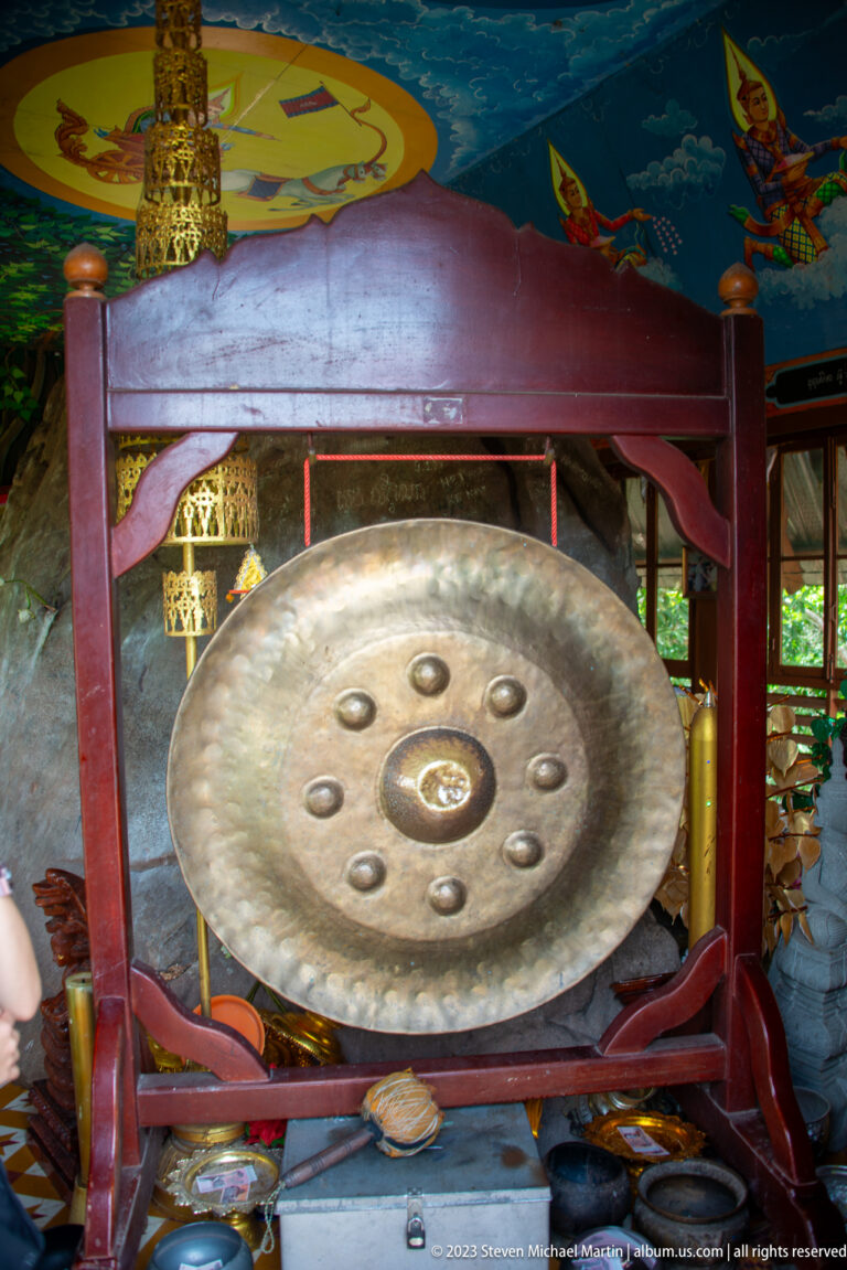 Large bronze gong with raised bosses suspended in a red wooden frame.