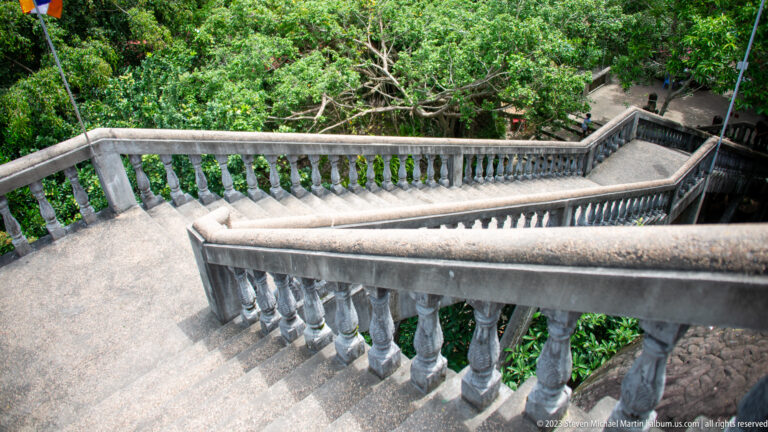 Long concrete stairway with balustrades descending through dense trees.