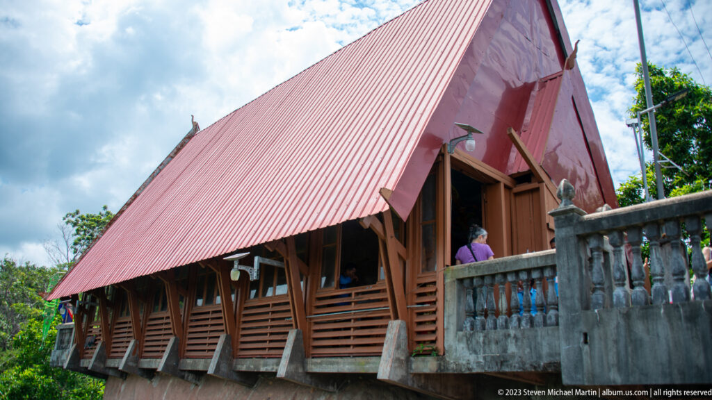 Side view of a long wooden hall beneath a steep red metal roof.