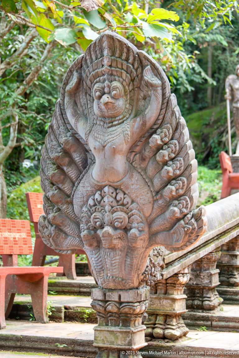Weathered carved naga balustrade terminal with layered serpent hoods and floral ornament.