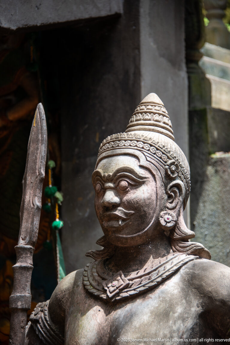 Crowned muscular guardian statue holding a broad-bladed spear.