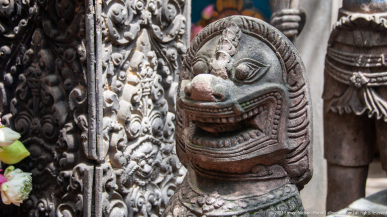 Open-mouthed carved guardian creature beside a richly ornamented doorway.
