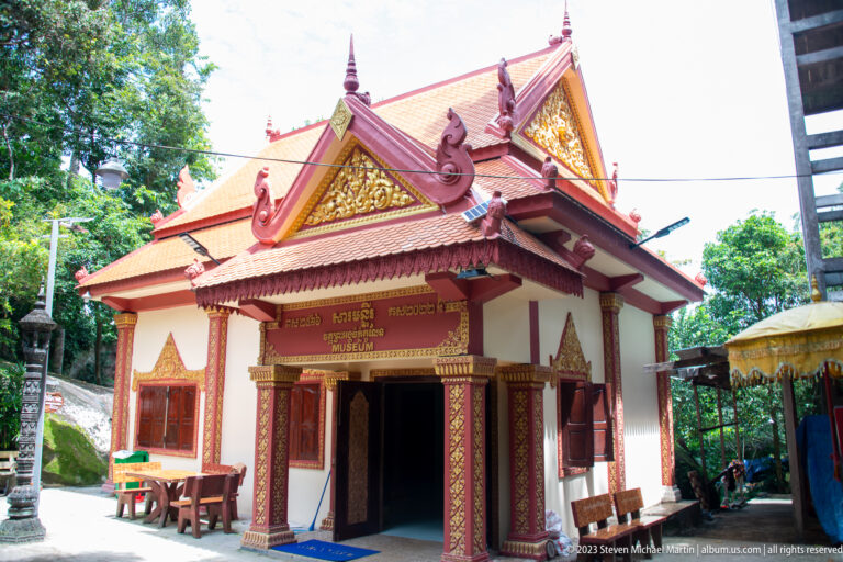 Small cream-and-red temple building with ornate gable and Khmer signage above the entrance.