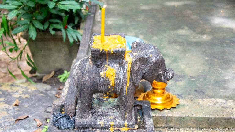 Small stone elephant covered in yellow wax with a lit candle on its back.