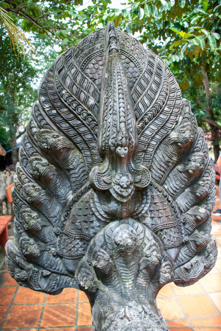 Frontal view of a broad multi-headed naga sculpture with dense carved scales.