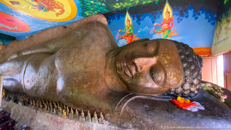 Full reclining Buddha beneath bright blue murals with small votive figures along the base.