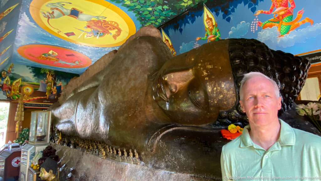Visitor standing beside the monumental reclining Buddha beneath painted ceiling murals.