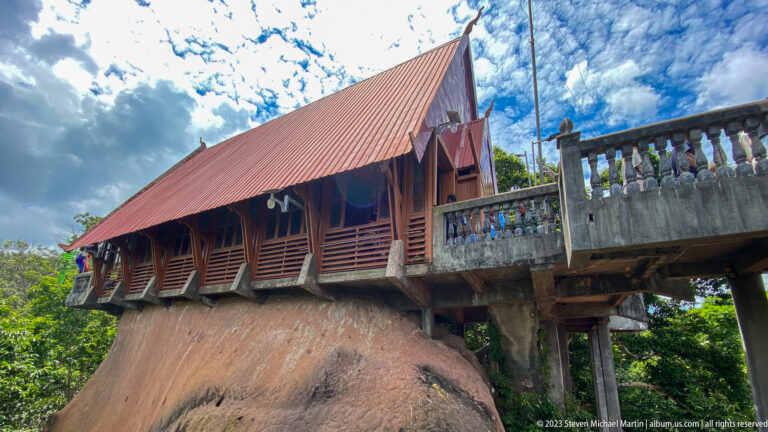 Alternate exterior view of a wooden temple hall built above exposed rock.