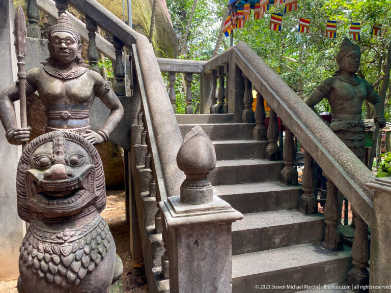 Standing guardian and seated lion beside a temple stairway.