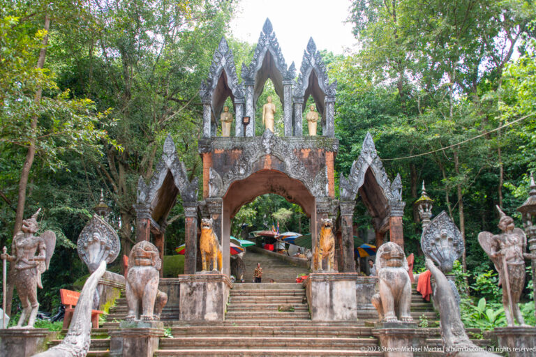 Frontal view of a stair gateway with Buddha niches, naga finials, and guardian statues.