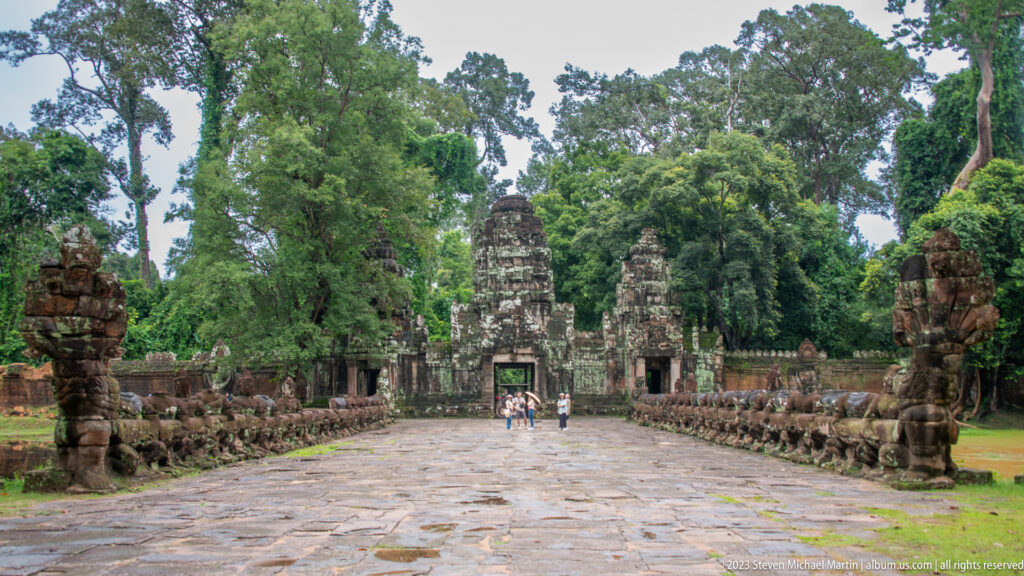 Centered paved causeway with rows of stone guardians leading to a weathered temple tower.