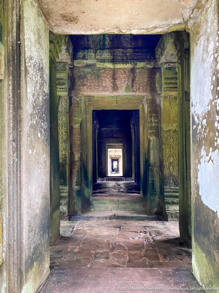 Long sandstone corridor of aligned rectangular doorways ending in a small square of daylight.