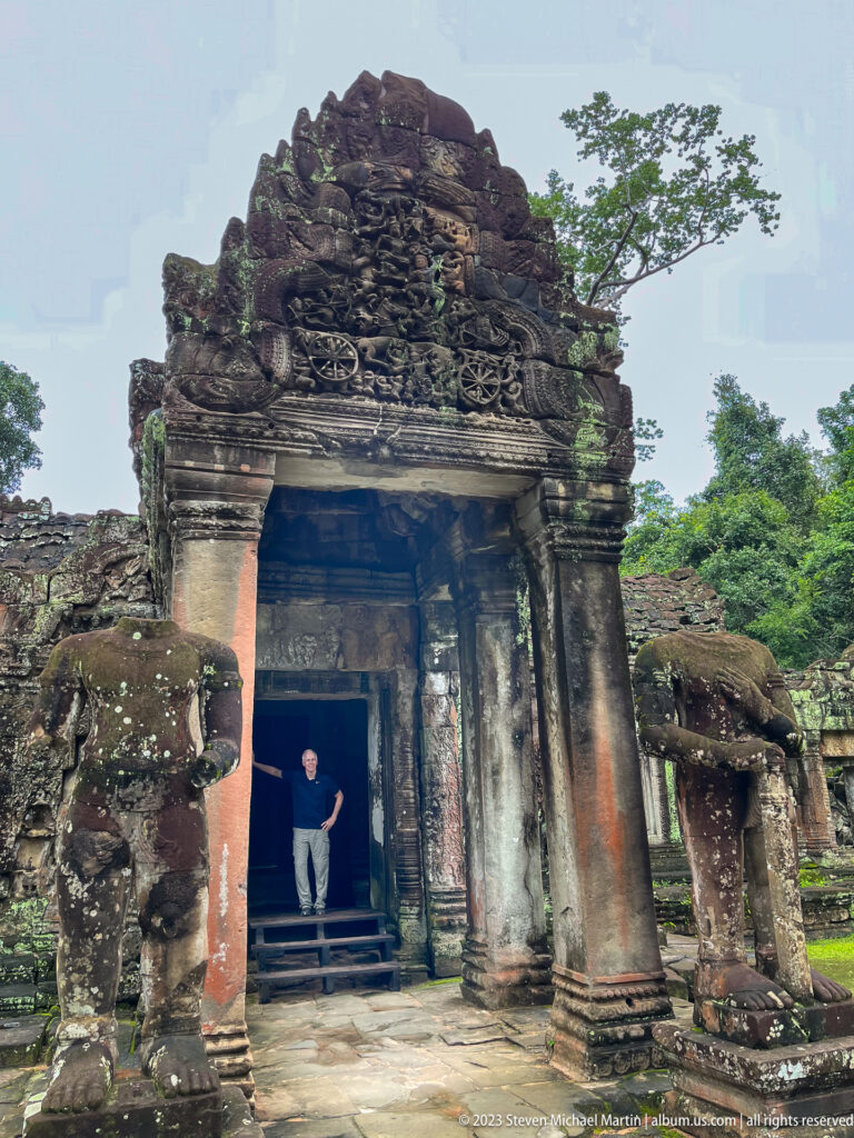 Large carved sandstone gateway with guardian figures and a visitor standing inside the dark passage.