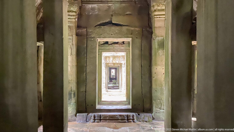 Narrow vertical view through several aligned sandstone doorways toward a bright passage.