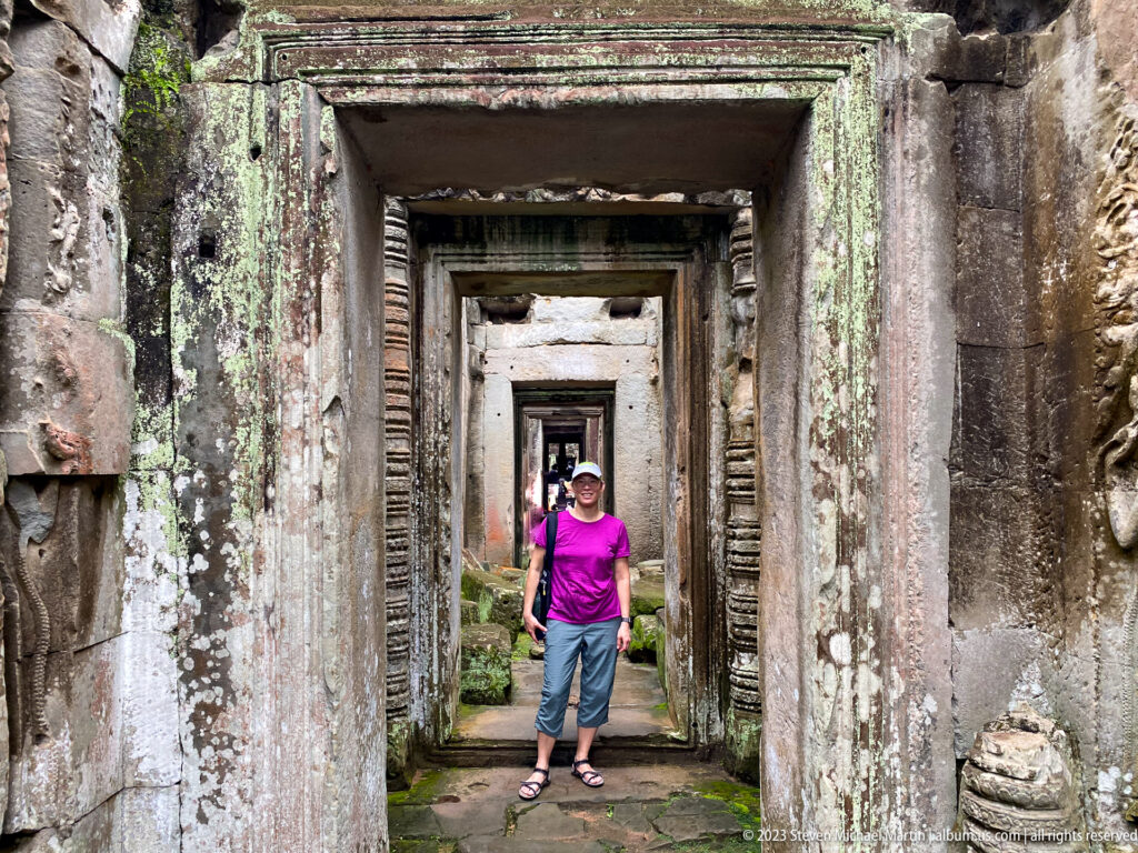 Female visitor standing within several aligned sandstone doorways in a weathered temple corridor.
