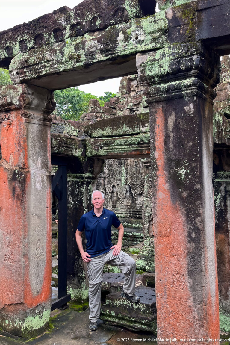 Male visitor posing beneath a low sandstone gallery supported by massive round columns.