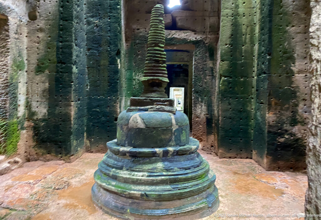 Tiered stone stupa centered in a dark chamber with aligned doorways glowing behind it.