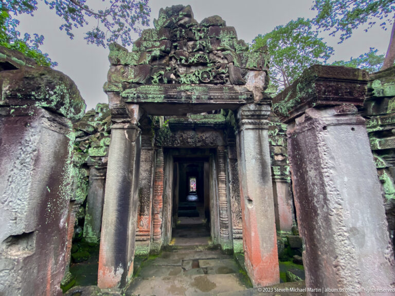 Carved sandstone doorway with round columns and a long dark passage aligned beyond.