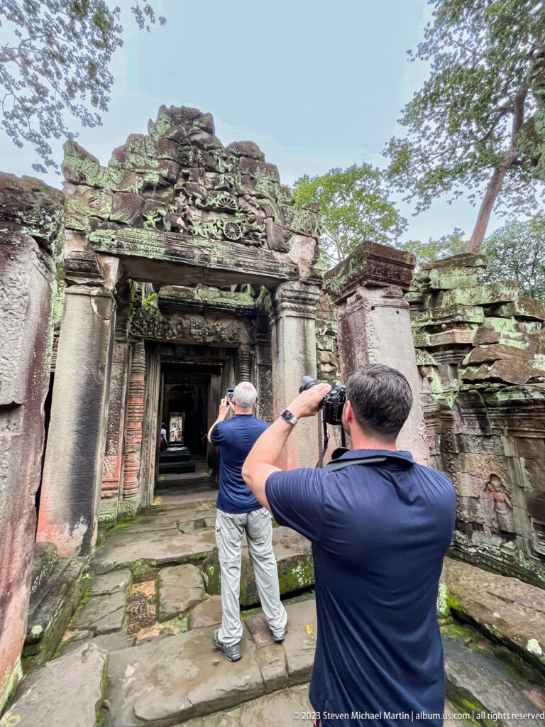 Two male visitors photographing and examining a carved sandstone temple entrance.