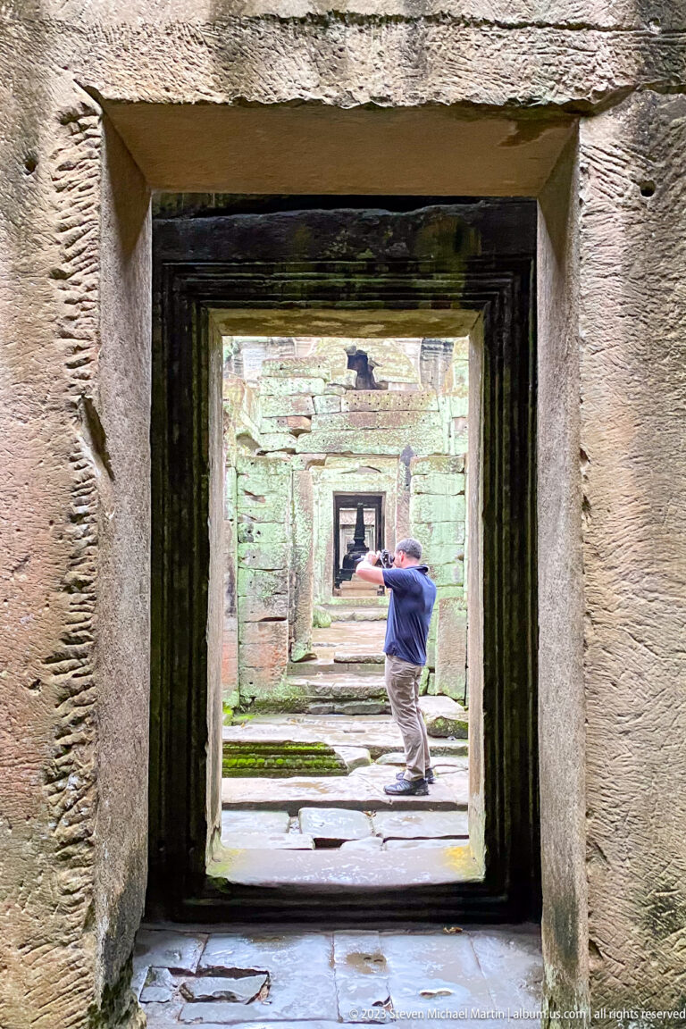 Male visitor photographing in a courtyard, framed by dark nested sandstone doorways.