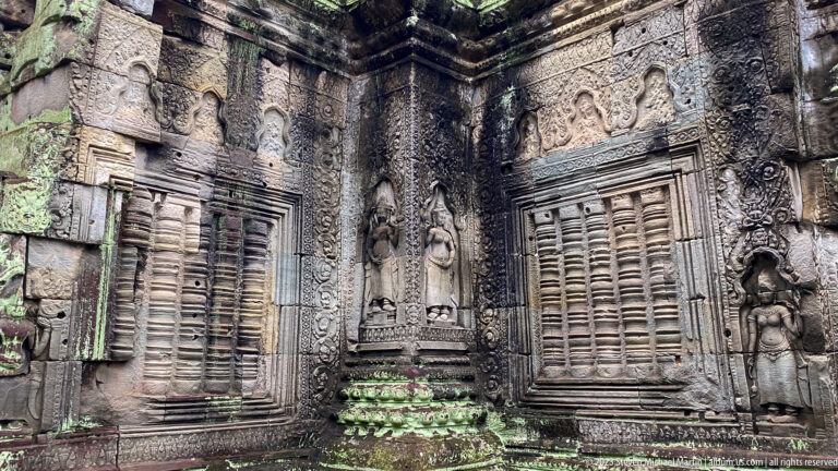 Decorated sandstone corner with two blind windows, standing female figures, and dense carved ornament.
