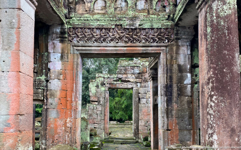 Carved sandstone doorway with a figure frieze and another ruined doorway visible beyond.
