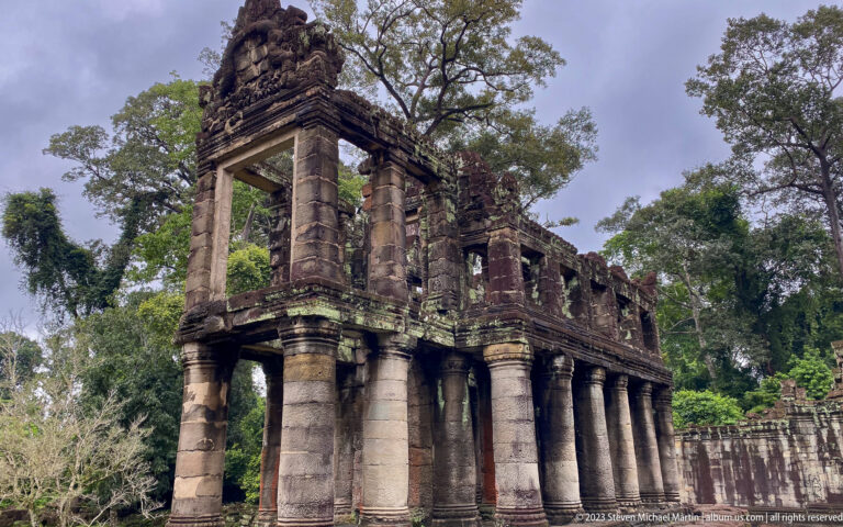 Corner view of a two-story sandstone building with heavy columns and large upper openings.