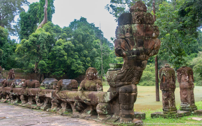 Large guardian beside a row of kneeling stone figures supporting a long serpent-shaped balustrade.