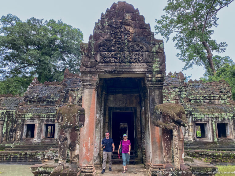 Two visitors walking beneath a large carved gateway flanked by elephant guardians.