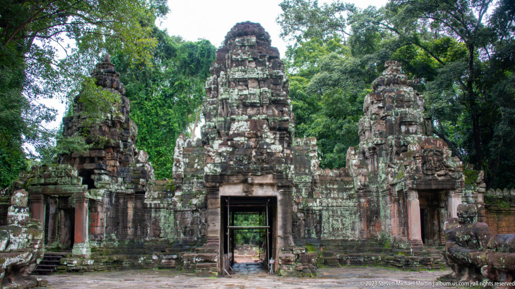 Frontal view of a weathered multi-towered stone gateway with a dark central doorway.