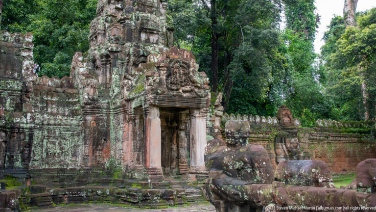 Oblique temple gateway with carved towers and a weathered guardian sculpture in the foreground.