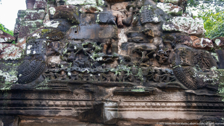 Close view of an ornate Khmer stone relief with figures, scrollwork, and symmetrical carved bands.
