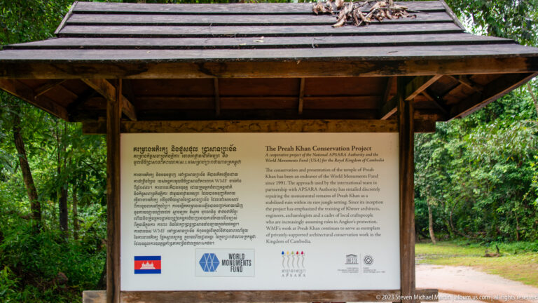 Roofed bilingual sign titled The Preah Khan Conservation Project with institutional logos below.