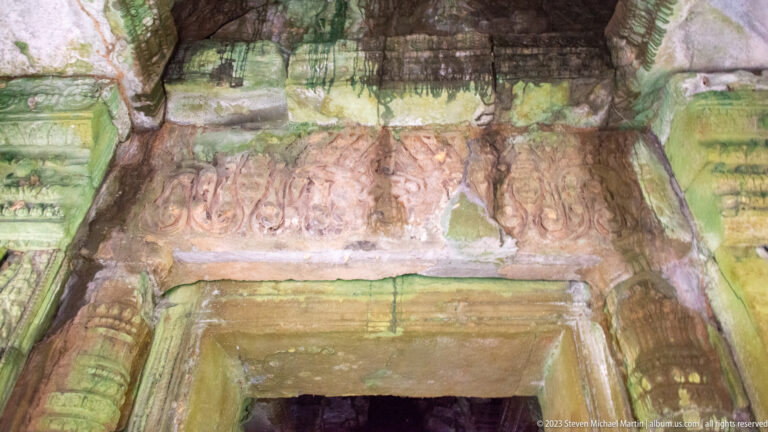 Weathered stone lintel above a doorway with a row of small carved human figures.