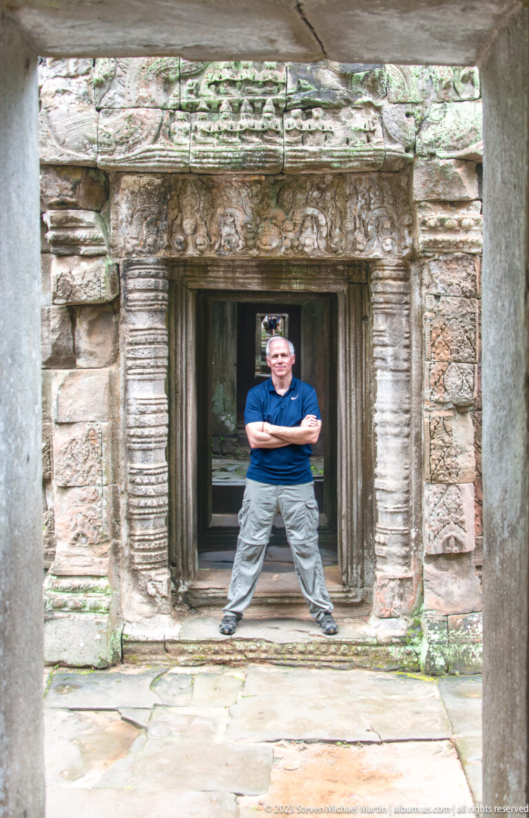 Visitor standing with arms crossed inside a carved sandstone doorway with layered lintels and pilasters.