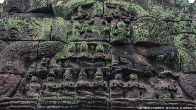 Close view of a weathered central relief with stacked carved figures and surrounding scrollwork.