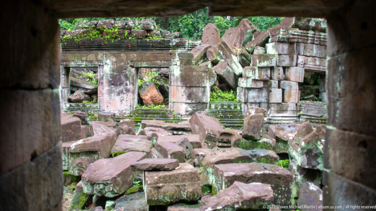 View through a dark doorway into a ruined chamber filled with fallen sandstone blocks and broken masonry.