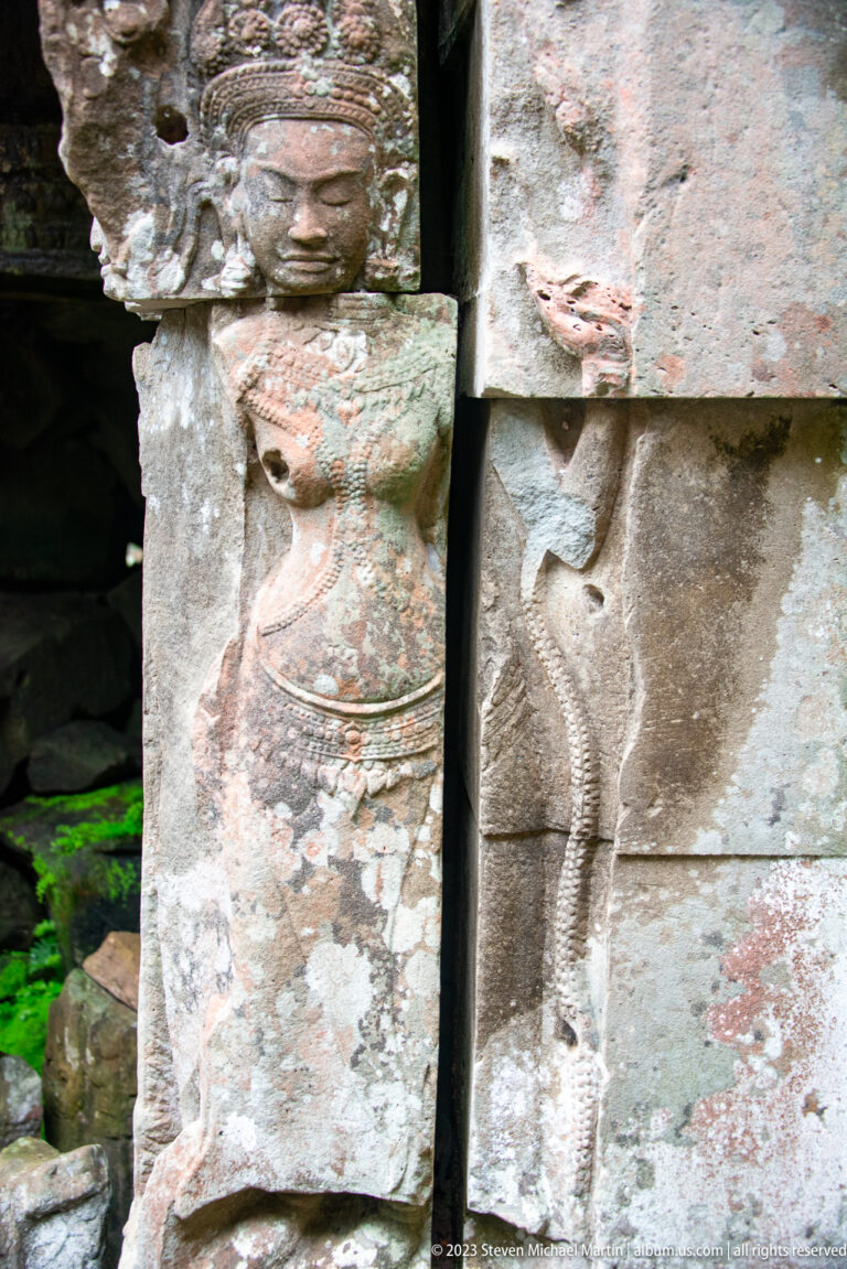 Weathered standing female relief carved beside a stone doorway jamb.