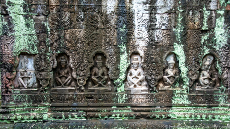 Row of seated stone figures in ornate arched niches across a weathered temple wall.