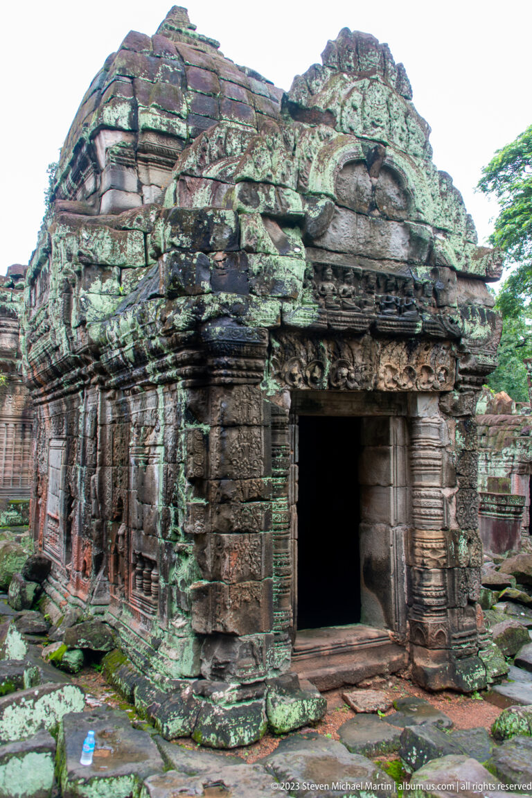 Small weathered sandstone shrine with a dark doorway, low roof, and lichen-covered walls.
