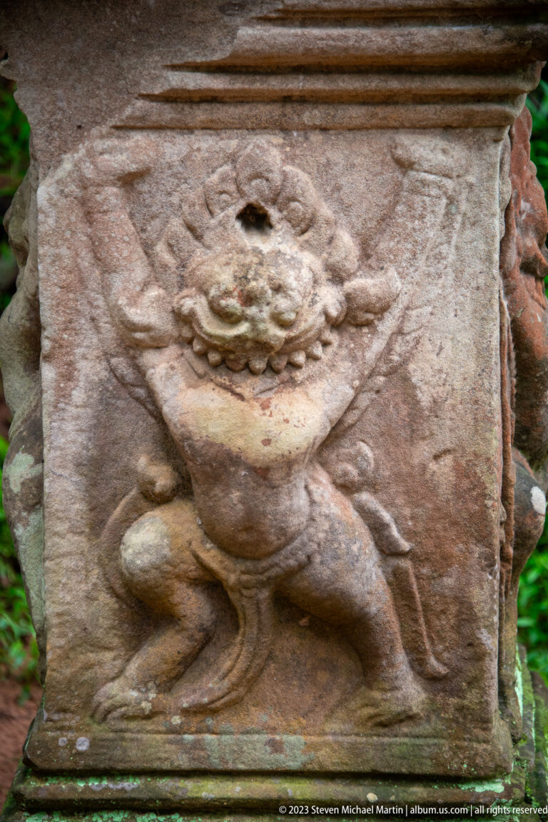 Weathered lion-like guardian relief carved on the front of a square sandstone pedestal.