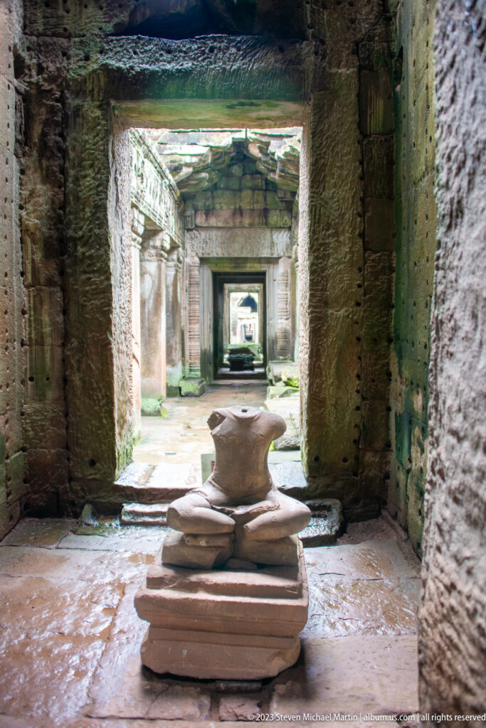 Broken stacked stone monument centered in a roofless chamber with a long line of doorways beyond.